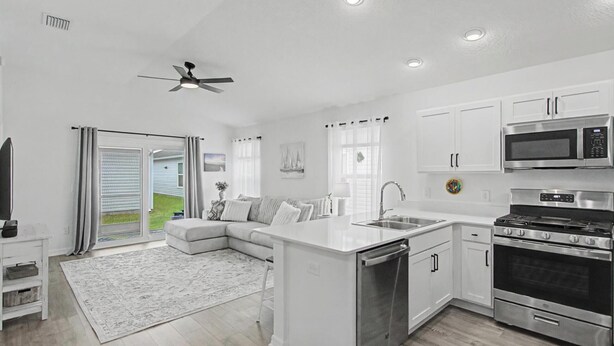 A modern kitchen with white cabinetry, a built-in dishwasher, a stove, and a microwave. - New Villa Beautifully Furnished Eastport Golf Cart Included (Sumterville)