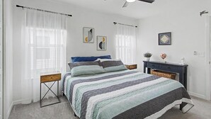 A bedroom with a bed, a nightstand, a dresser, a ceiling fan, and two wall art pieces. - New Villa Beautifully Furnished Eastport Golf Cart Included (Sumterville)