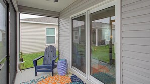 A covered porch with a ceiling fan, a sliding glass door, a blue Adirondack chair, and a patterned rug. - New Villa Beautifully Furnished Eastport Golf Cart Included (Sumterville)