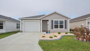 A single-story house with a garage, a front porch, and a small garden area with plants and a pathway. - New Villa Beautifully Furnished Eastport Golf Cart Included (Sumterville)