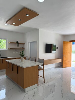 Una cocina moderna con una isla central, armarios de madera, un televisor integrado y una puerta que da a un espacio exterior.