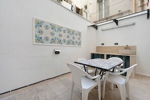 En hyggelig udendørs spiseplads med et bord, stole, flisebeklædt væg og en hængende lampe.