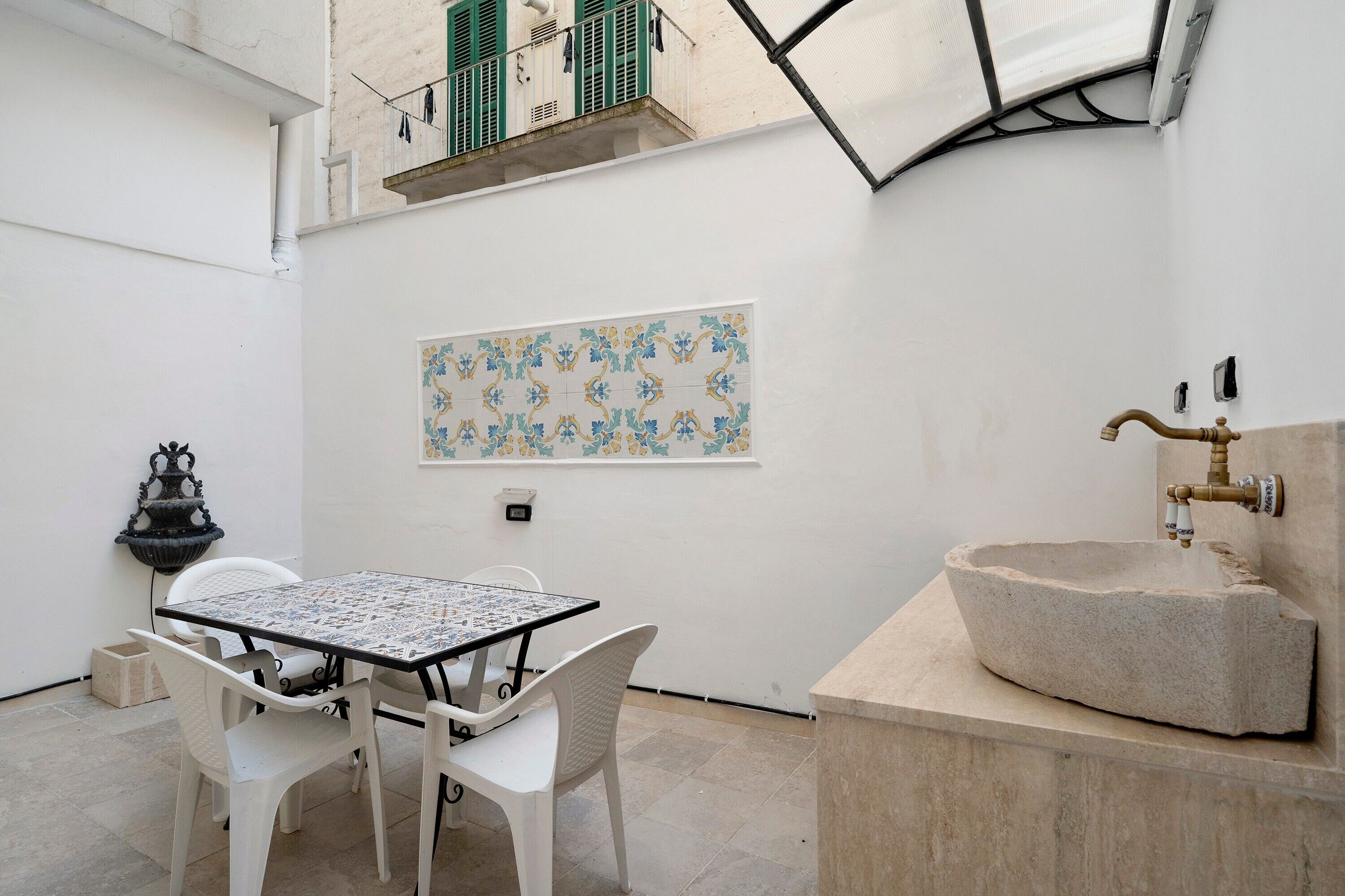 A small outdoor patio with a table and chairs, a decorative wall tile, a stone sink, and a hanging light fixture.