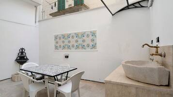 A small outdoor patio with a table and chairs, a decorative wall tile, a stone sink, and a hanging light fixture.