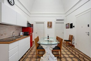 Eine kleine Küche mit weißen Schränken, einem roten Kühlschrank, einem Esstisch mit Glasplatte und Holzstühlen sowie einem gemusterten Boden.