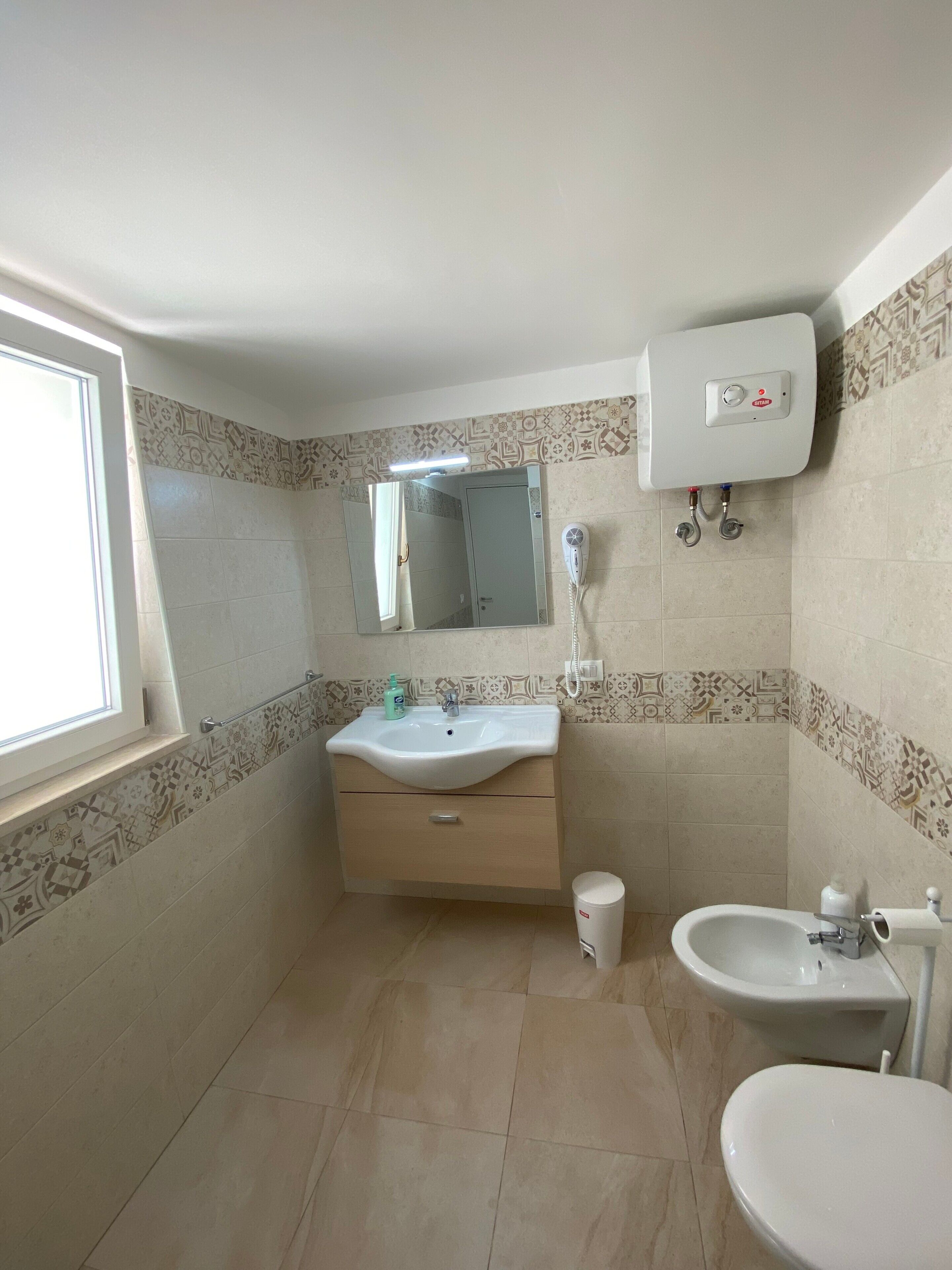 Ein Badezimmer mit Waschbecken, Spiegel, Toilette und einem Fenster.