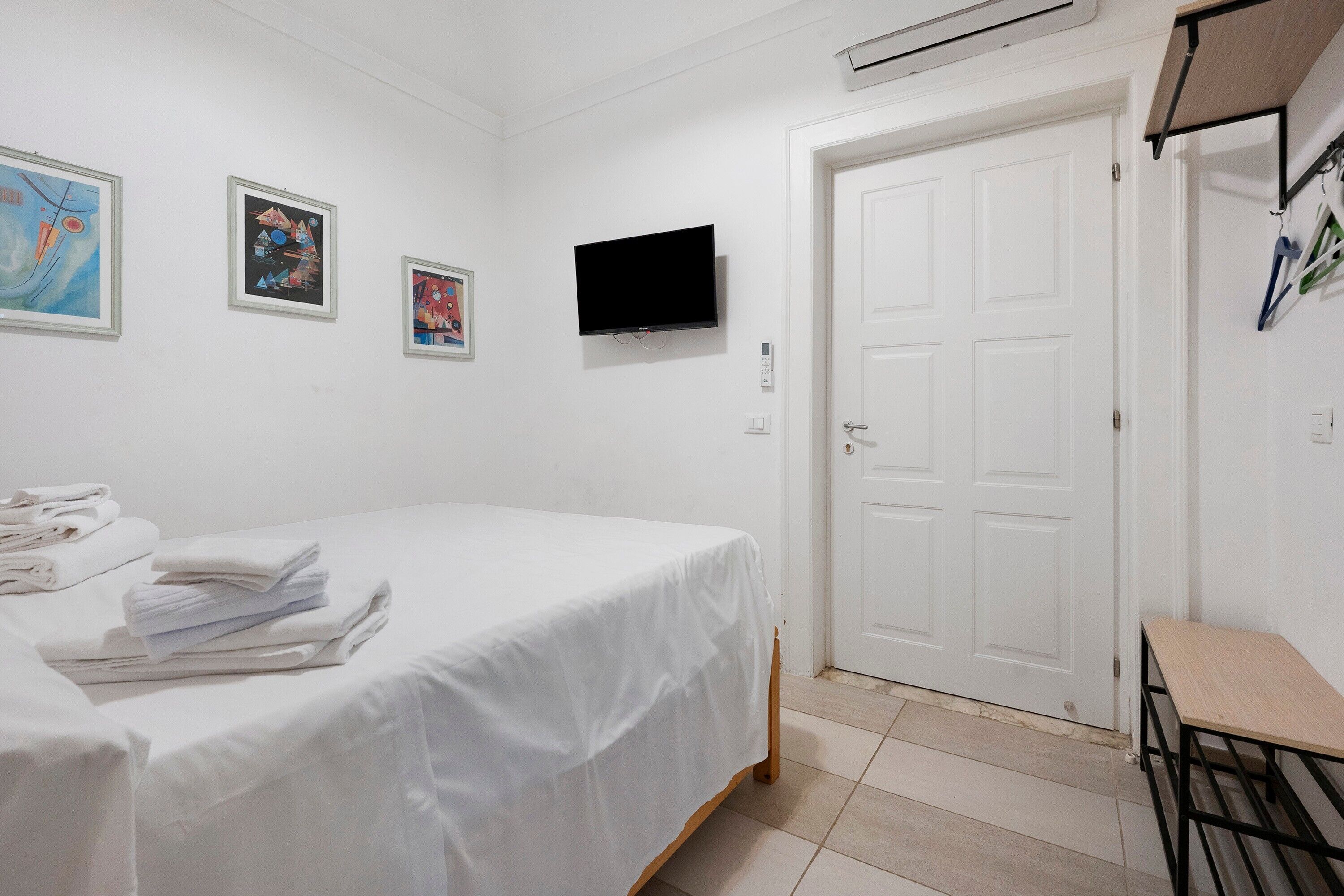 A hotel room with a bed, a flat-screen TV, a door, and artwork on the wall.