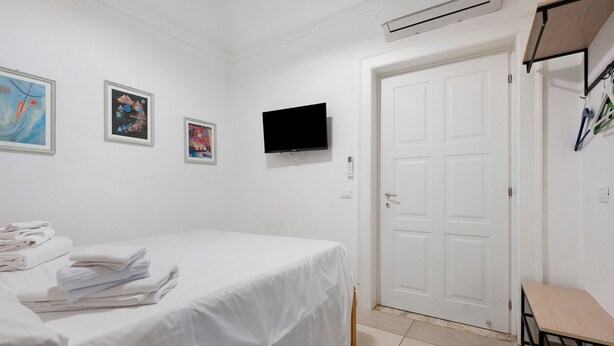 A hotel room with a bed, a flat-screen TV, a door, and artwork on the wall.