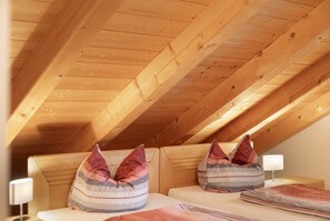 A room with a sloped ceiling and wooden beams, featuring two beds with striped pillows and a bedside table with a lamp. - Apartment 'Für 3 Personen 47 M²' with Sea View, Balcony and Wi-Fi (Egling)