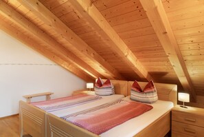 A bedroom with a sloped ceiling, wooden beams, a bed with pillows, a bedside table, and a nightstand. - Apartment 'Für 3 Personen 47 M²' with Sea View, Balcony and Wi-Fi (Egling)