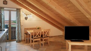 Un comedor con mesa y sillas de madera, un televisor sobre un mueble bajo y un ventanal con cortinas.