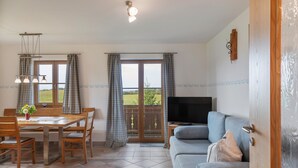 Un salon comprenant un canapé, une table à manger avec des chaises, un téléviseur et une vue à travers la porte vitrée.
