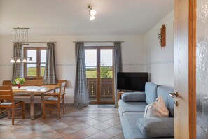Ein Wohnzimmer mit Sofa, einem Esstisch mit Stühlen, einem Fernseher und Blick durch die Glastür.