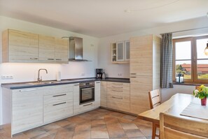 A modern kitchen with light wood cabinetry, a built-in oven, and a dining area with a table and chairs. - Apartment 'Für 2 Personen 53 M²' with Balcony and Wi-Fi (Egling)