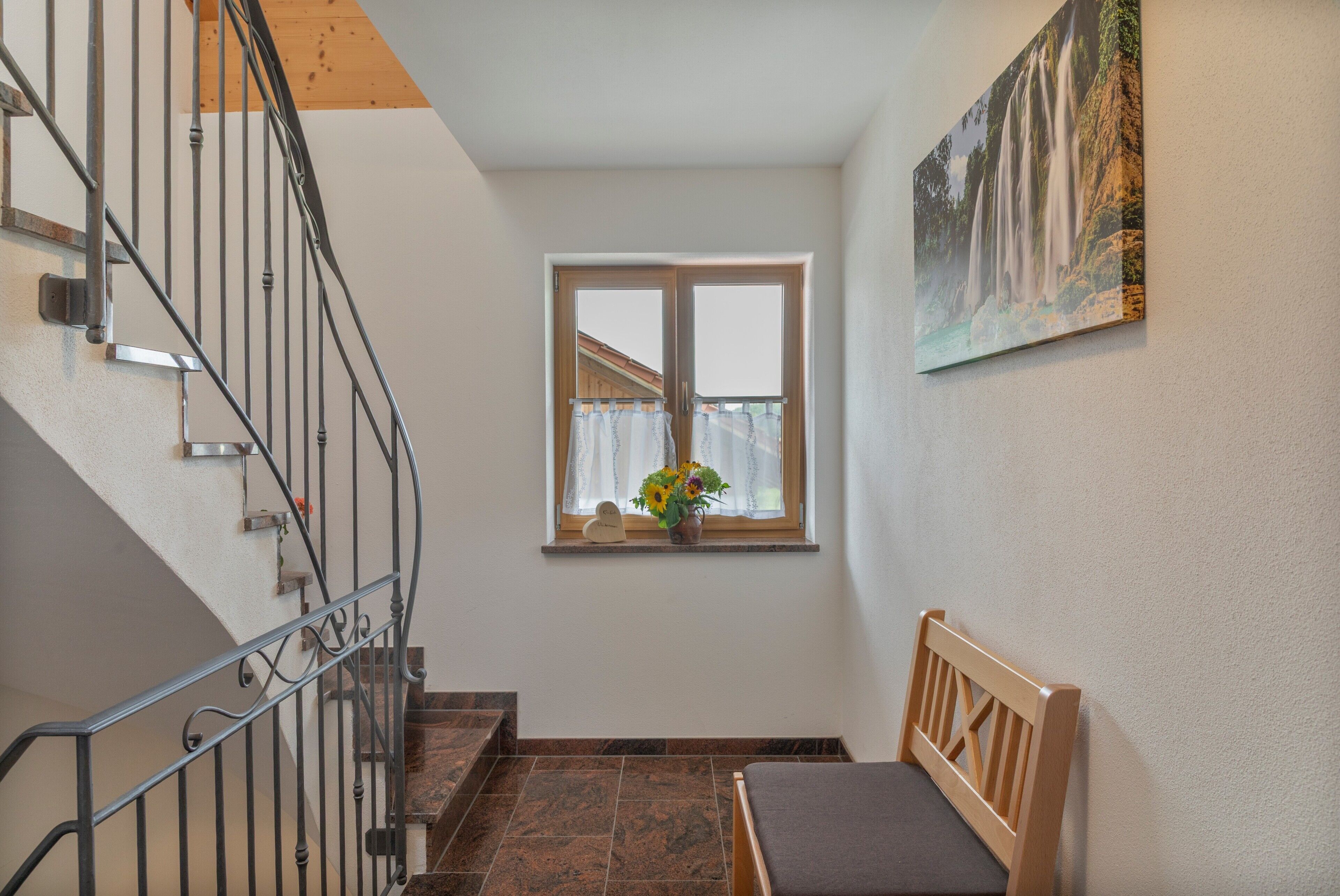 A staircase with metal railings leading to a landing with a window and a wooden bench.