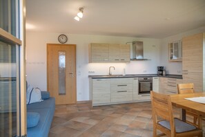 A modern kitchen with wooden cabinets, a built-in oven, and a dining area with a table and chairs. - Apartment 'Für 2 Personen 53 M²' with Balcony and Wi-Fi (Egling)
