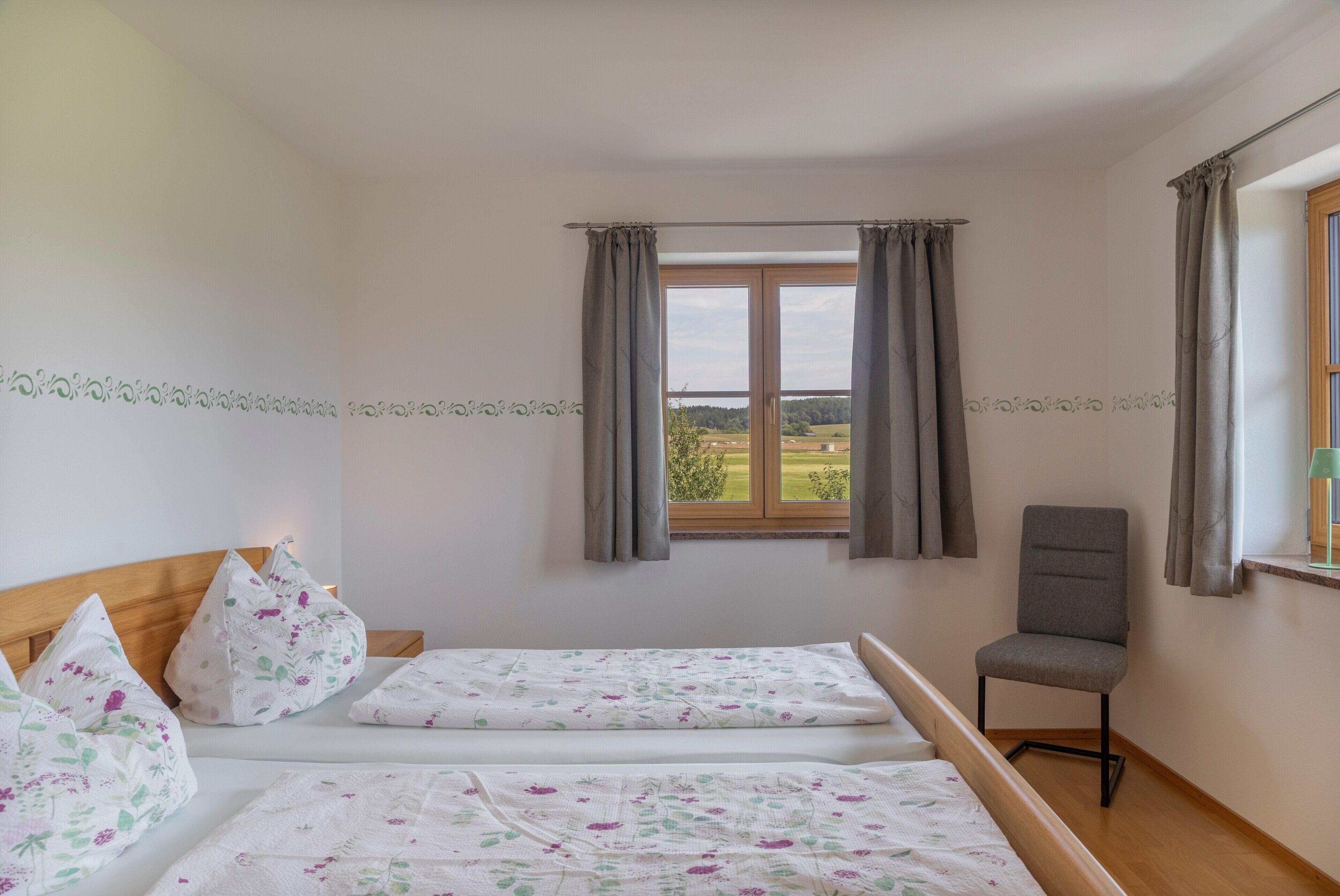 A bedroom with two beds, a chair, and a window with curtains.