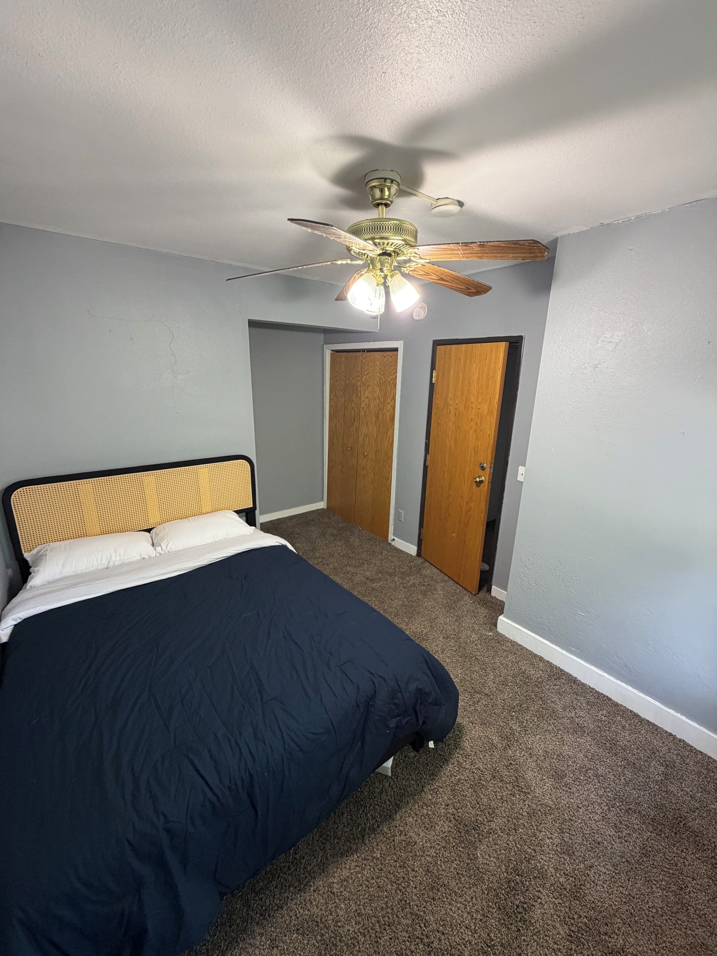 A bedroom with a bed, a ceiling fan, and two wooden doors.