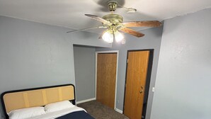 A bedroom with a bed, a ceiling fan, and two wooden doors.