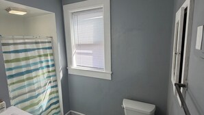A bathroom with a toilet, a shower curtain, a window, and a sink.