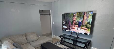 Una sala de estar con un sofá modular, un televisor de pantalla plana, un ventilador de techo y un tapete estampado.