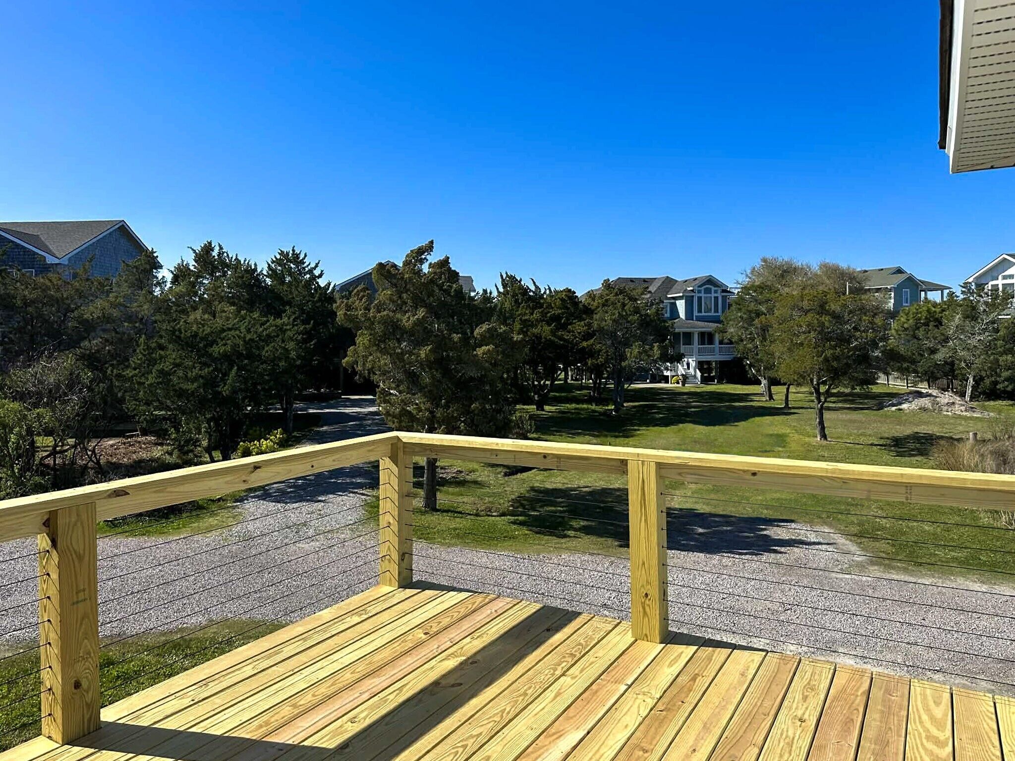 Une terrasse en bois avec une rambarde, un chemin de gravier et des maisons en arrière-plan.