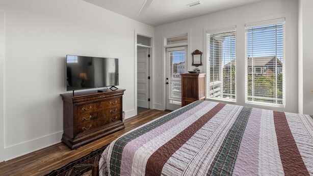 A bedroom with a bed, a dresser, a television, a ceiling fan, and large windows. - Wyf of Bathe: Silver Lake Views with docking available. (Ocracoke)