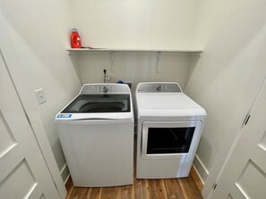 A laundry room with two white washing machines and a shelf above them.