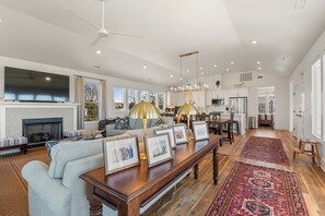 A spacious living room with a fireplace, a large flat-screen TV, and a dining area with a chandelier.