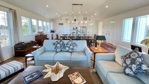A spacious living room with a light blue sofa, a coffee table, and a dining area in the background. - Wyf of Bathe: Silver Lake Views with docking available. (Ocracoke)