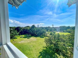 A view from a window overlooking a well-maintained lawn, a white building, and a lighthouse in the distance.
