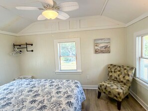 A bedroom with a bed, a chair, a ceiling fan, a window with blinds, and a wall-mounted coat rack. - Ocracoke Local 4: Harbor Views | Private Boat Slip | King Bed (Ocracoke)