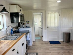 Uma cozinha compacta com armários brancos, micro-ondas, pia e lixeira.