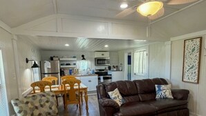 Una sala de estar con sofá de cuero marrón, sillón estampado y una zona de comedor con sillas y mesa de madera.