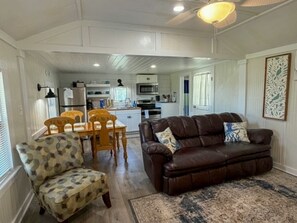 Ein Wohnzimmer mit braunem Ledersofa, einem gemusterten Sessel und einem Essbereich mit Holztischen und -stühlen.
