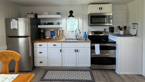 Cocina compacta con armarios blancos, un refrigerador de acero inoxidable, un microondas, un horno y un lavamanos.