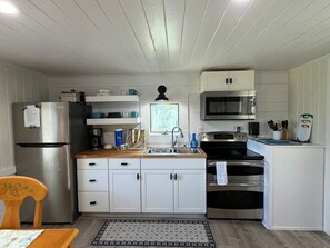 Eine kleine Küche mit weißen Schränken, einem Edelstahlkühlschrank, einer Mikrowelle, einem Backofen und einem Spülbecken.