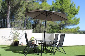 Eine Terrasse im Freien mit Tisch und Stühlen, einem großen Sonnenschirm und einem Blumentopf.