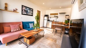 A living room with a sofa, coffee table, and a kitchen area with a dining table and chairs. - Idylle apartment – Sleeps 2, with a large terrace and a view (Pertuis)