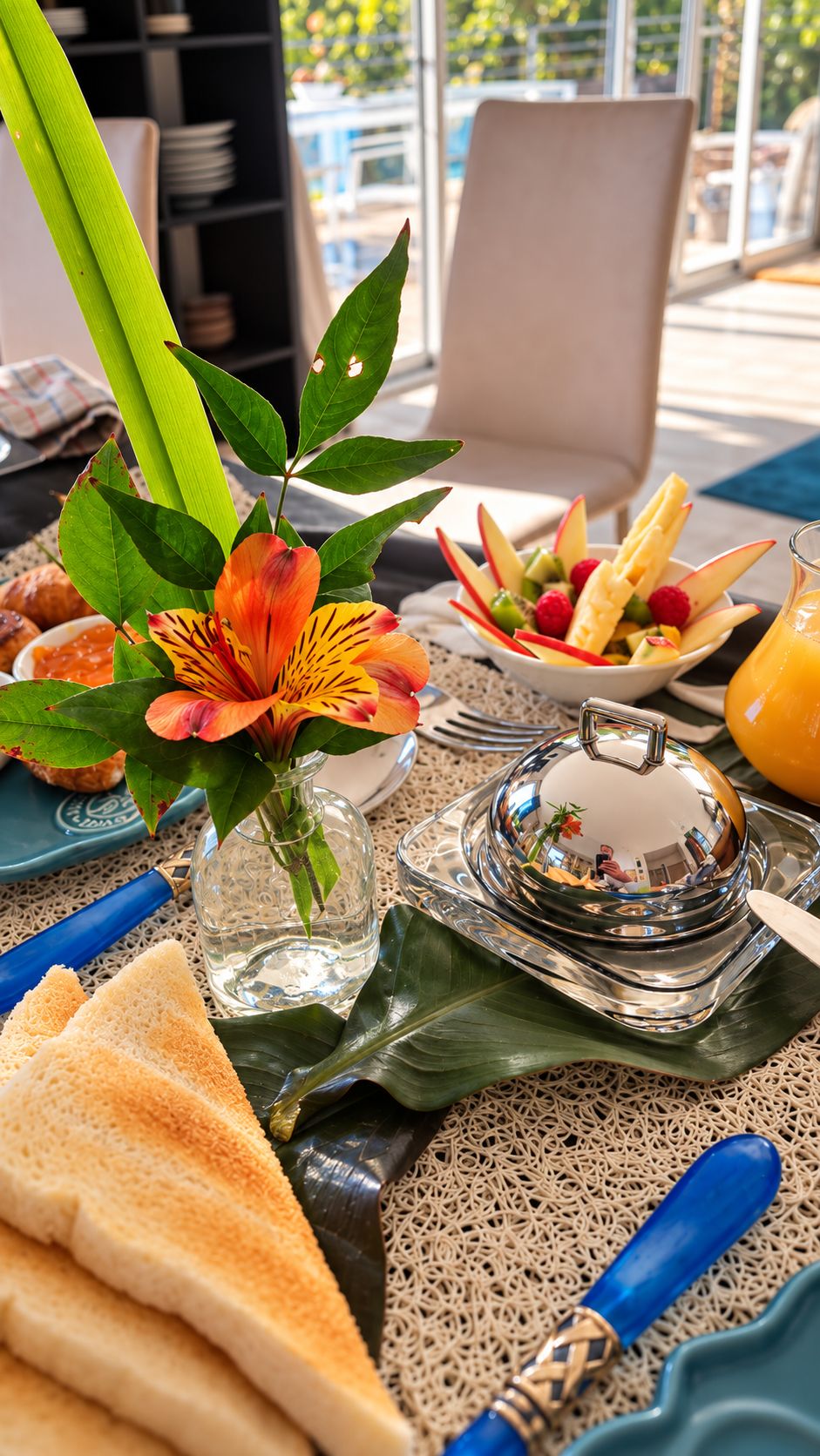 A table set with a variety of food items, including bread, fruit, and a decorative flower arrangement.