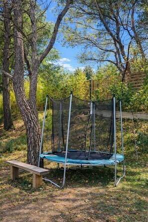 Un trampolí en un jardí d'estiu amb arbres i una tanca de fusta.