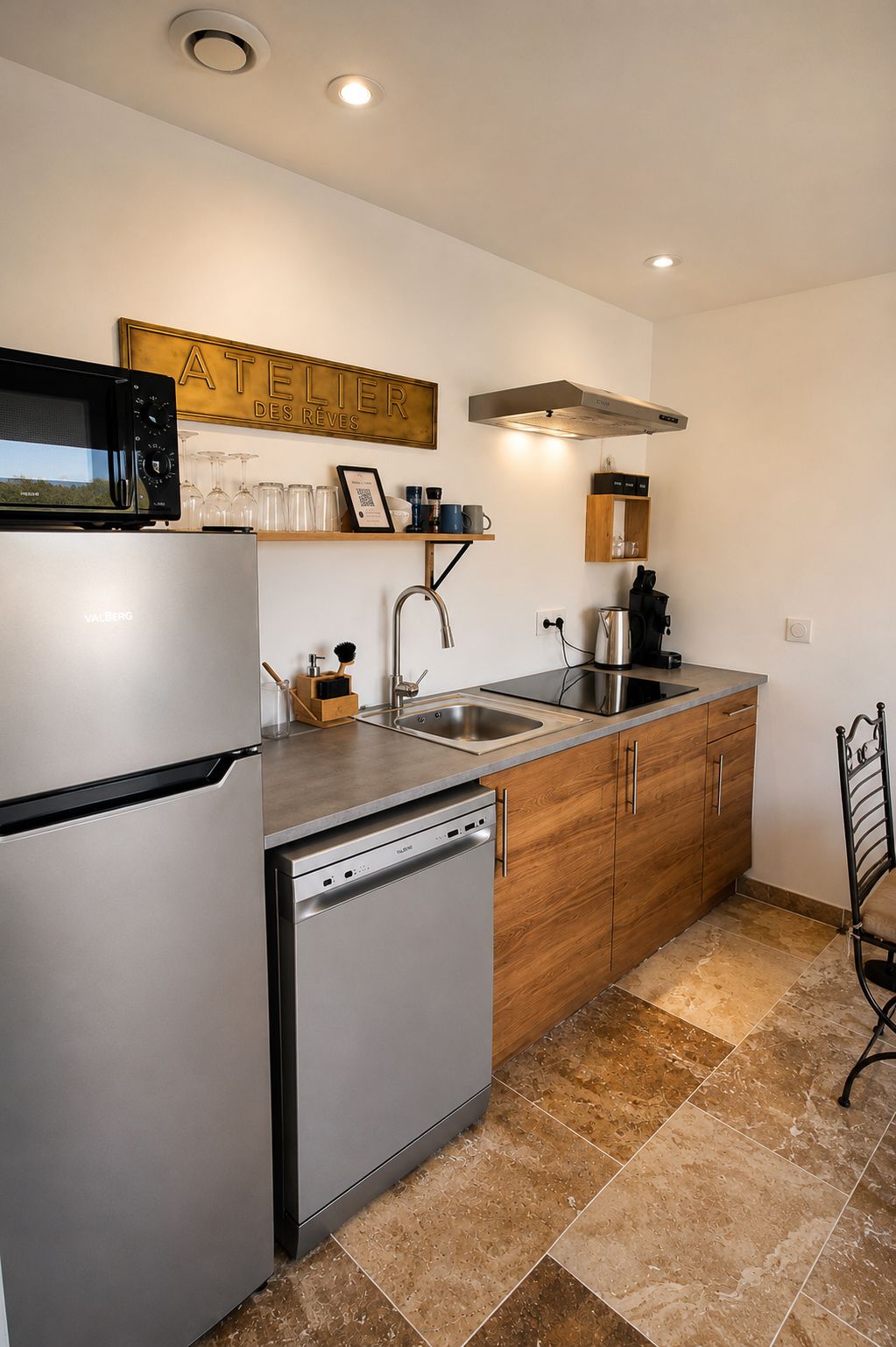 Una cocina compacta con un refrigerador de acero inoxidable, lavavajillas, pileta y armarios de madera.