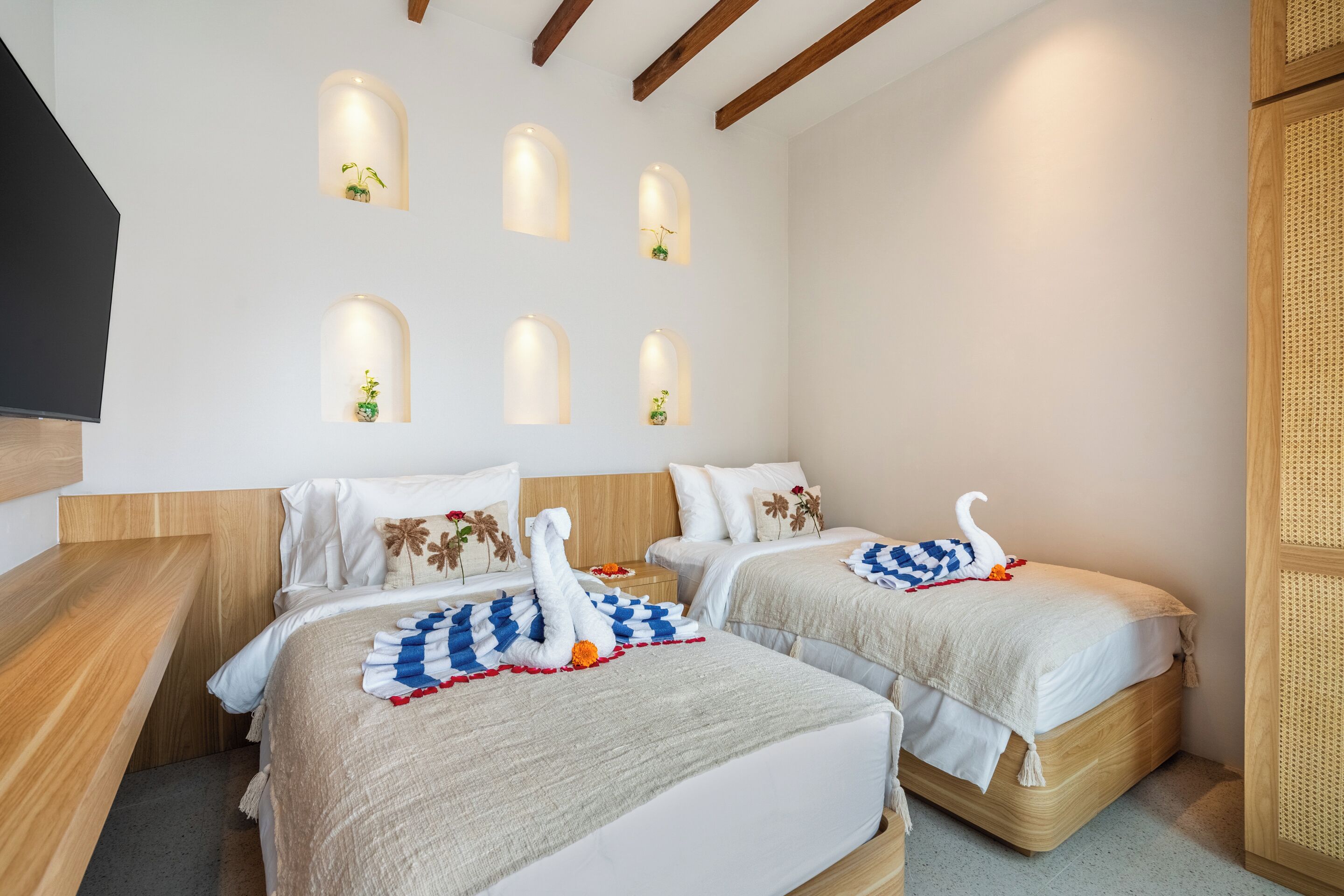Habitación de hotel con dos camas, cabecera de madera, televisión de pantalla plana y apliques de pared con plantas.