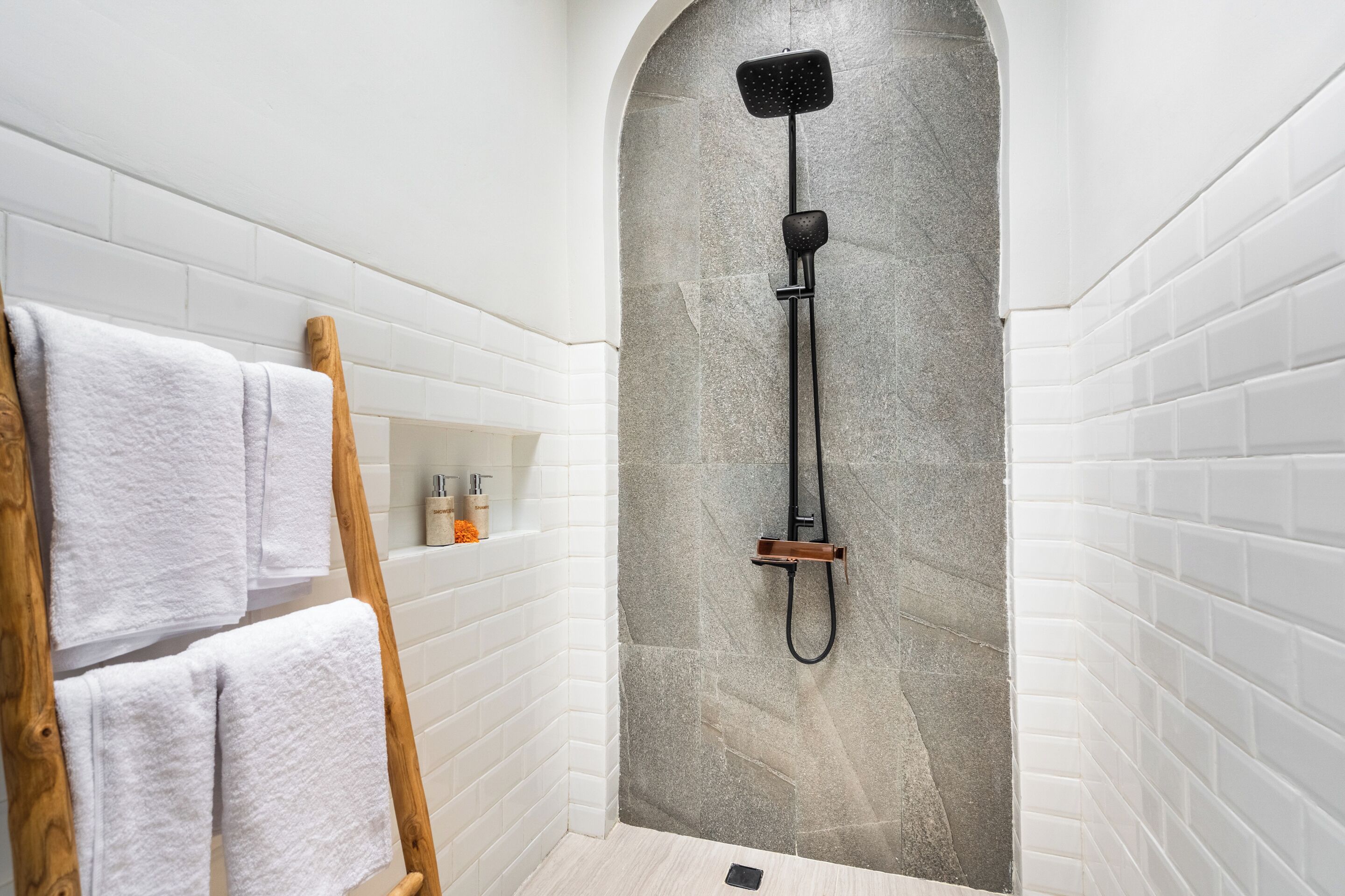 Una zona de ducha con pared de piedra, paredes de azulejos blancos y una escalera de madera.