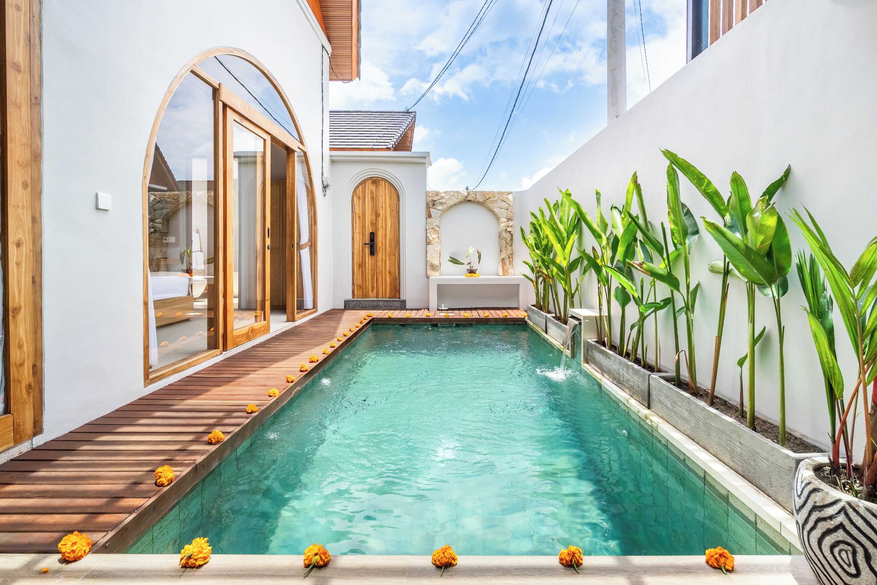 Piscina com deck de madeira, rodeada por paredes brancas e um arco de pedra.