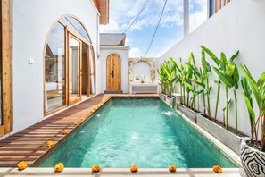 Una piscina con cubierta de madera, rodeada de paredes blancas y un arco de piedra.