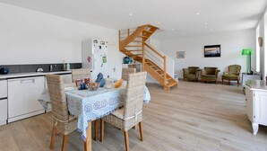 A modern kitchen with a dining area, a wooden staircase, and a living space with seating. - Ty Glas Guesthouse – Ground Floor Room (Pleubian)