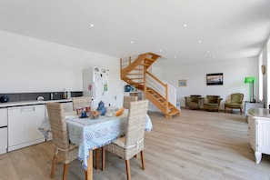 Una cocina moderna con comedor, una escalera de madera y una sala de estar con asientos.