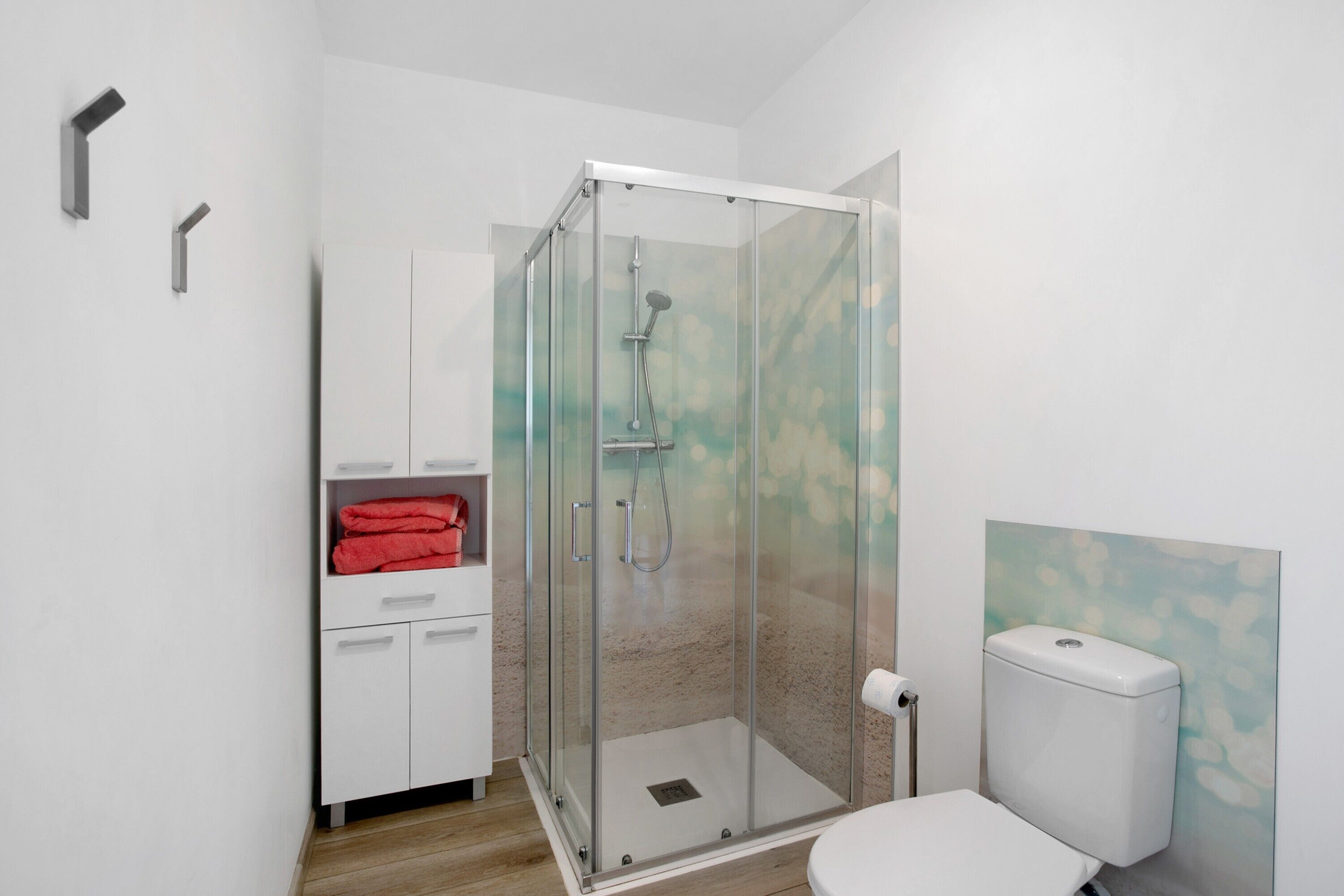 A modern bathroom with a glass-enclosed shower, white cabinets, a toilet, and a towel rack with red towels.