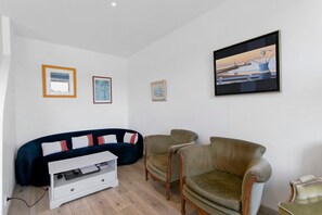 Una sala de estar con un sofá azul oscuro, dos sillones, un mueble blanco para televisión y cuadros enmarcados en la pared.